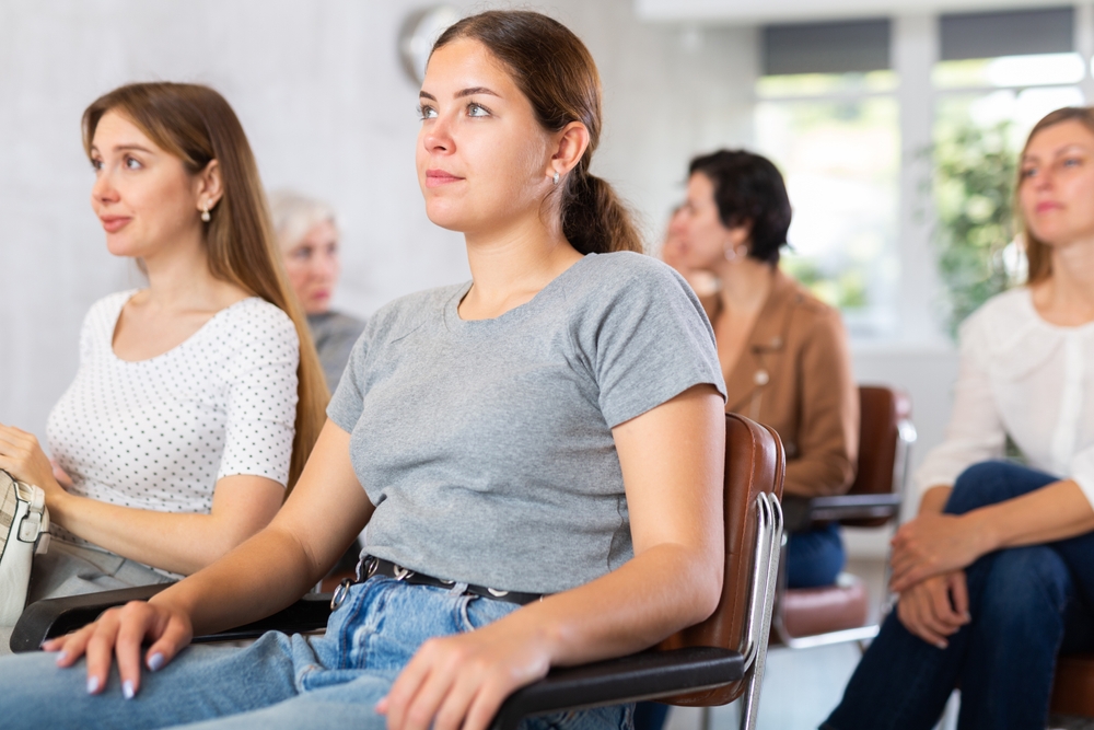 Interested,Positive,Young,Girl,Sitting,In,Group,Auditorium,And,Listening